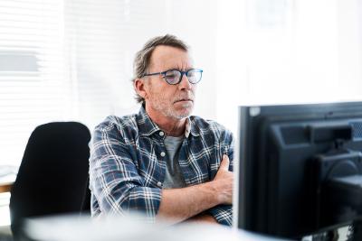 Mand over 40 år, som sidder og kigger på en computerskærm med sine skærmbriller på