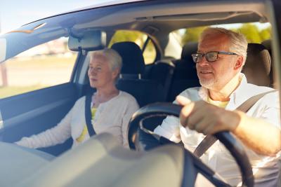 Ældre mand og kvinde i en bil, manden der kører bilen har almindelige afstandsbriller  på fordi man må ikke køre bil med læsebriller eller skærmbriller.