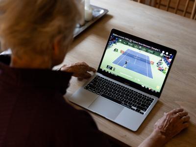 Ældre kvinde som sidder ved et bord og ser tenniskamp