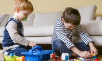 To børn der sidder på gulvet og leger med lego.